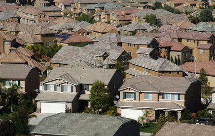 An aerial view of a suburban neighborhood featuring rows of similar two-story houses with garages and tiled roofing, closely packed together, showcases the uniformity and quality of residential roofing throughout the community.